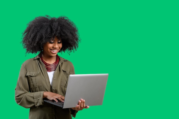 Donna che tiene il computer portatile durante la digitazione sulla tastiera, giovane donna afro america, su sfondo verde