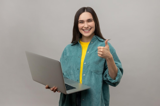 Woman holding laptop and showing thumbs up while talking on video call having online conference