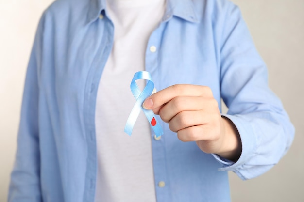 Woman holding light blue ribbon with blood drop closeup World Diabetes Day