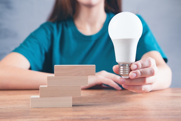 Woman holding a light bulb near the stairs made of wooden rectangles