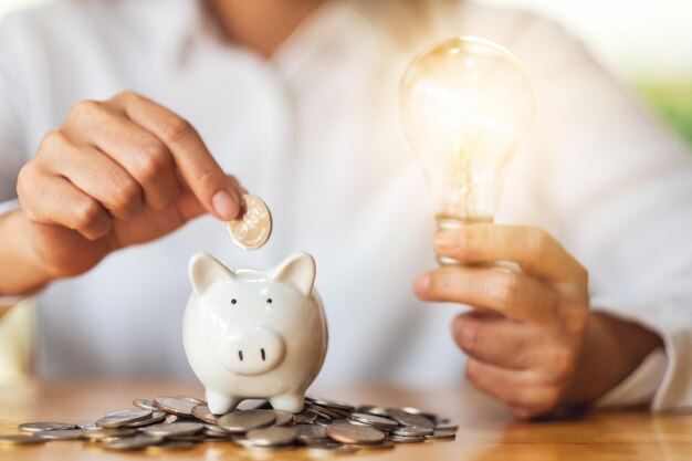 A woman holding light bulb while putting coins into piggy bank for saving money concept