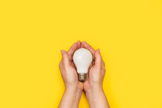 Woman holding a lightbulb with both hands on a yellow background