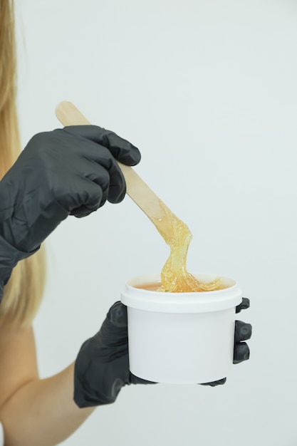 Woman holding liquid yellow paste for shugaring against white, copy space