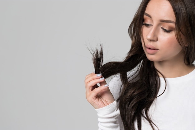 Woman holding and looking at split ends of her damaged long hair.