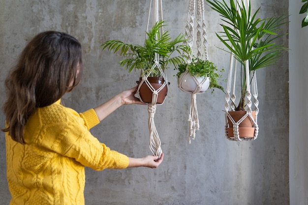 Woman holding macrame plant hanger with houseplant over grey wall