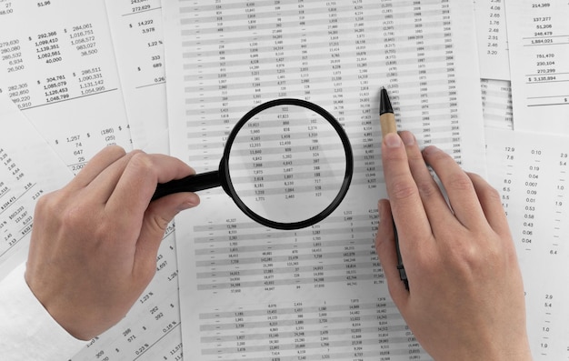 Woman holding a magnifying glass pointing at numbers on financial documents oncept of finance search and accounting