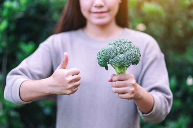 Una donna che tiene e fa il pollice in alto per mostrare un buon segno a un broccolo verde