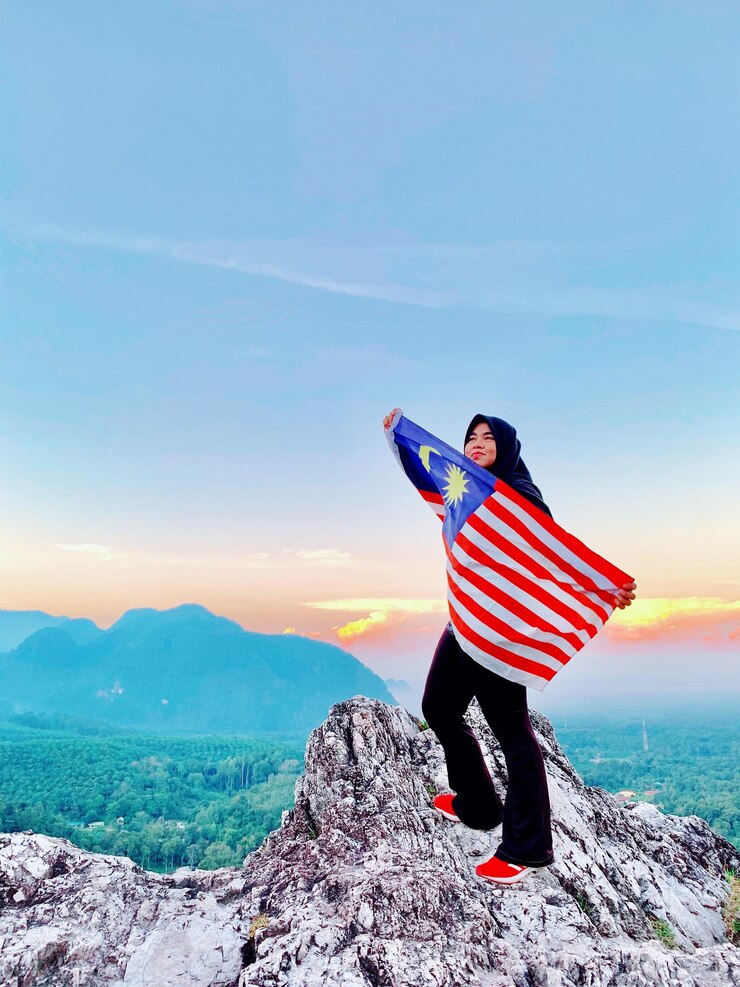 Photo 一位女士拿着马来西亚国旗,在日落时站在天空的山上
