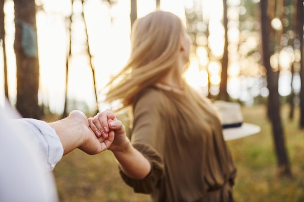 Woman holding man's hand Happy couple is outdoors in the forest at daytime