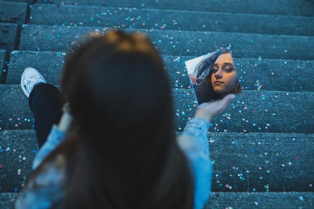 Woman holding mirror on staircase with multi colored confetti