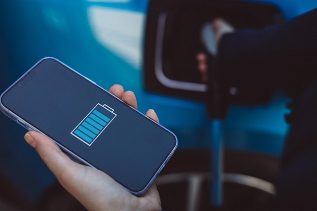 Photo woman holding mobile phone checking percentages of charged electric car