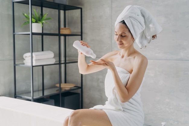Женщина держит бутылку-макет с натуральной косметикой по уходу за кожей в ванной комнате по уходу за телом