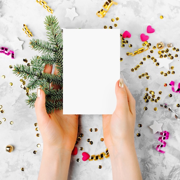 Woman holding mockup card with fir branch . Flat lay, top view