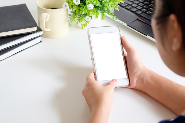 Woman holding mockup mobile phone on office desk.