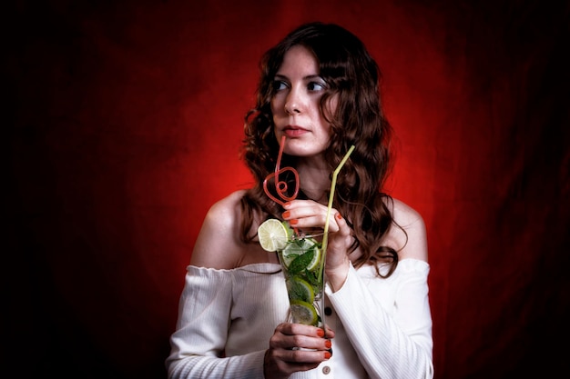 A woman holding a mojito cocktail in her hands on a red background