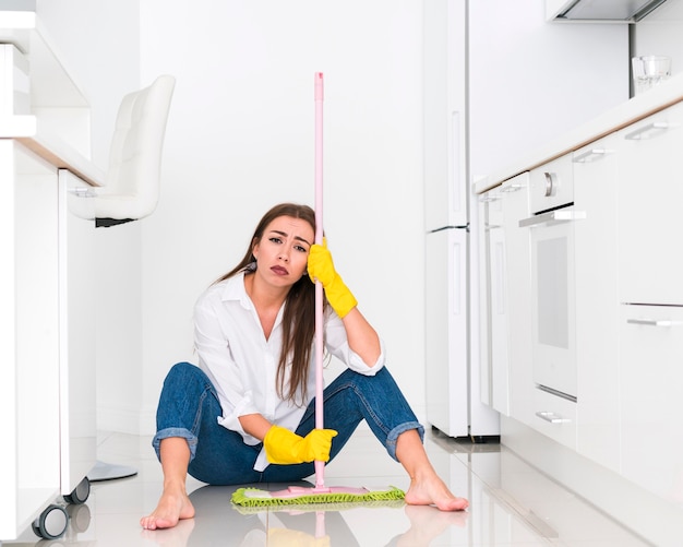 Woman holding a mop and sitting on the floor