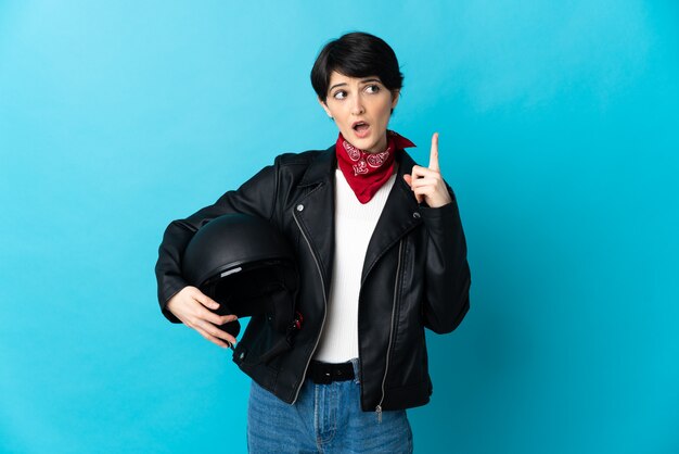 Woman holding a motorcycle helmet isolated on blue background thinking an idea pointing the finger up