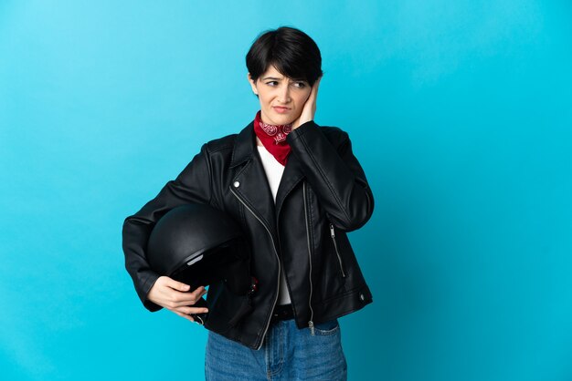 Donna che tiene un casco del motociclo isolato sullo spazio blu frustrato e che copre le orecchie