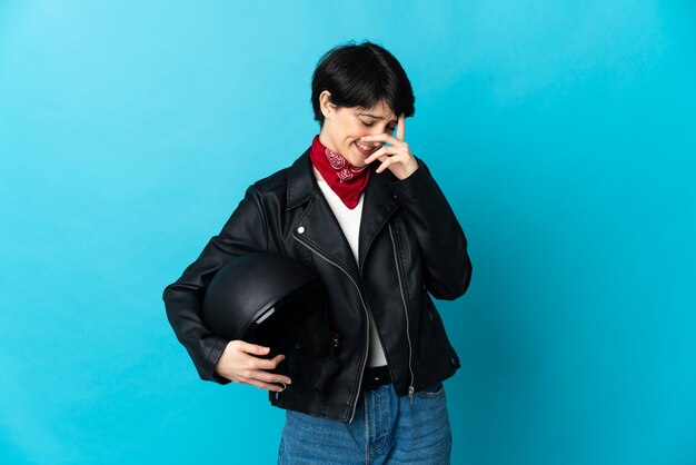 Woman holding a motorcycle helmet isolated on blue wall laughing