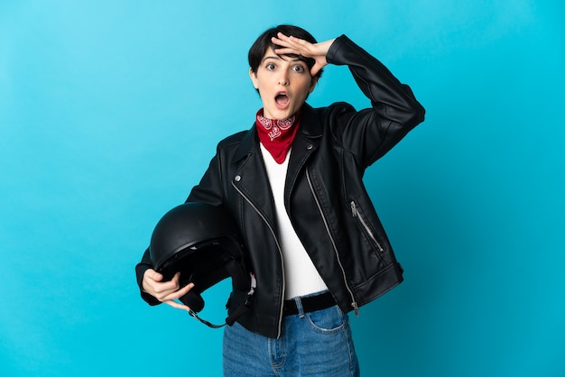 Woman holding a motorcycle helmet isolated doing surprise gesture while looking