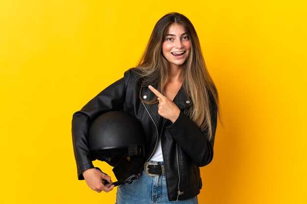 Donna che tiene un casco da motociclista isolato sulla parete gialla che punta di lato per presentare un prodotto