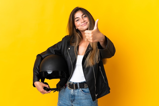 Foto donna che tiene un casco da motociclista isolato sulla parete gialla con i pollici in su perché è successo qualcosa di buono