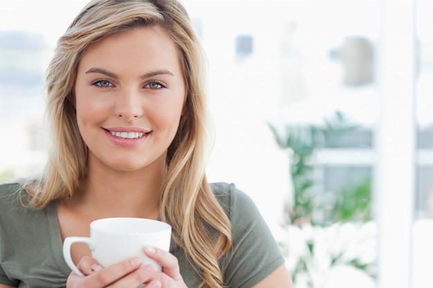 Woman holding a mug in her hands and smiling, while looking forward