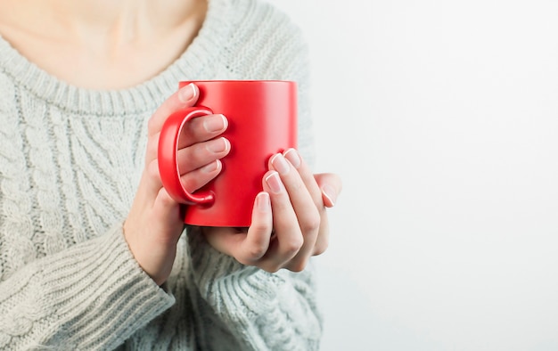 灰色の背景に彼女の手で熱いお茶のマグカップを保持している女性