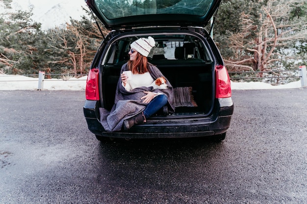 写真 車のトランクに犬と一緒に座っているカップを握っている女性