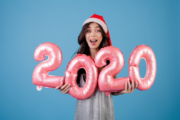 Woman holding new year balloons wearing santa hat and dress