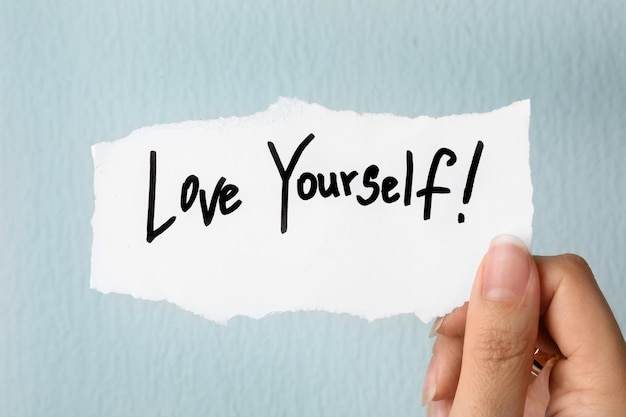 Photo woman holding note with words love yourself on light background closeup