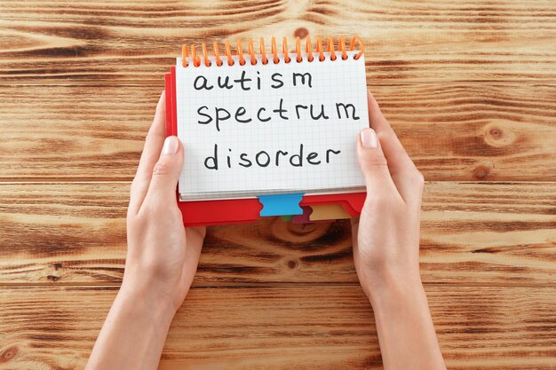 Woman holding notepad with text autism spectrum disorder on wooden background