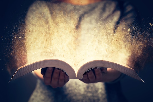 Женщина с открытой книгой в двух руках Свет, выходящий из книги, как концепция обучения, образования, знаний и религии
