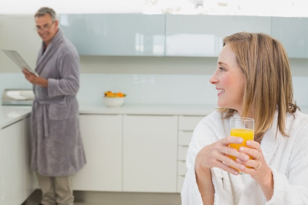 Woman holding orange juice with man in background