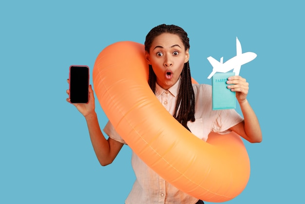 Woman holding orange rubber ring paper plane and mobile phone with empty screen vacation abroad