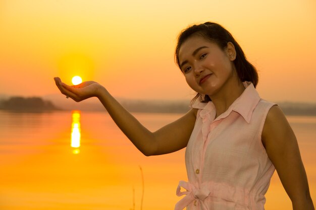 Woman holding orange while standing against sky during sunset