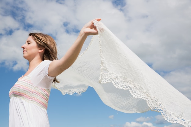 Woman holding out scarf against blue sky and clouds