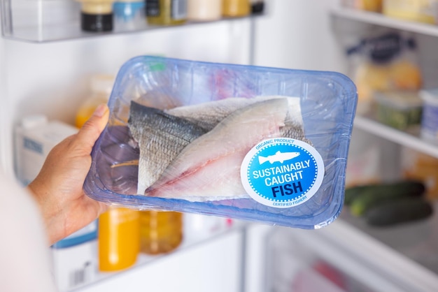 Woman holding package of responsibly caught fresh fish concept\
of sustainable fishing