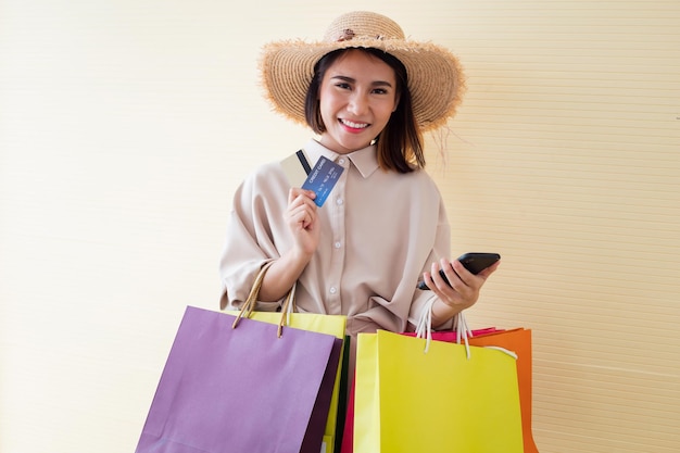 Donna che tiene sacchetti di carta e carta di credito con un sorriso su sfondo giallo nel concetto di shopping