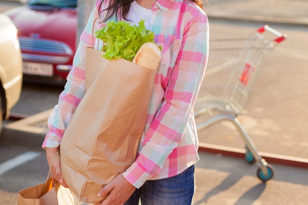 Woman holding paper bags with groceries near a supermarket. 