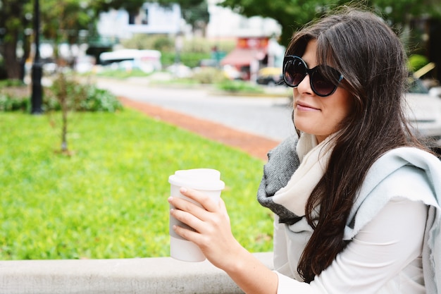 Woman holding paper coffee cup in the street.