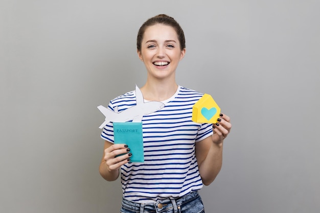 Woman holding paper house and passport relocating to a new house abroad buying real estate