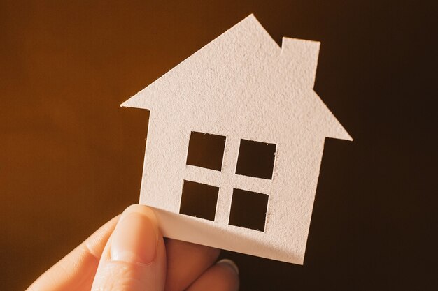 Woman holding a paper house with her hands backlit on a dark space