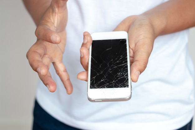 Foto donna che tiene il telefono che ha lasciato cadere lo schermo, rotto nella mano, molto triste.