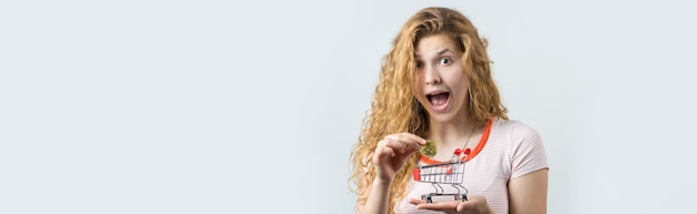 Woman holding a physical bitcoin in her hand on gray background Emotional portrait of a girl with cryptocurrency