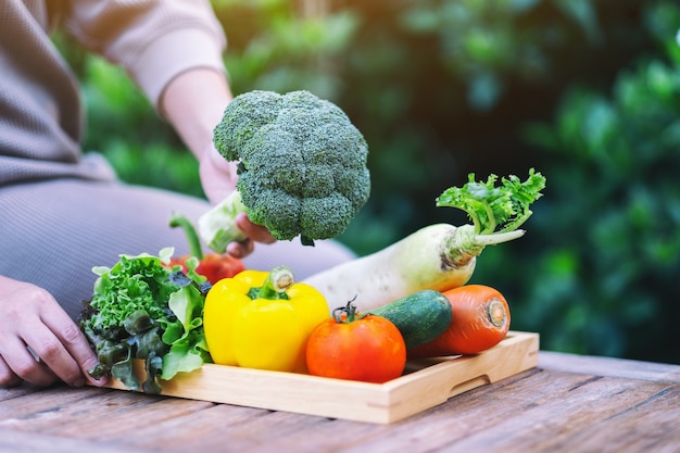 Una donna che tiene e raccoglie verdure miste fresche da un vassoio di legno sul tavolo