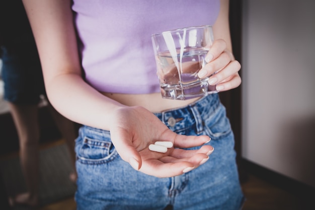 Woman holding pill and glass of water in hands taking emergency medicine