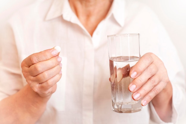 woman holding a pill and a glass of water in her hands close-up
