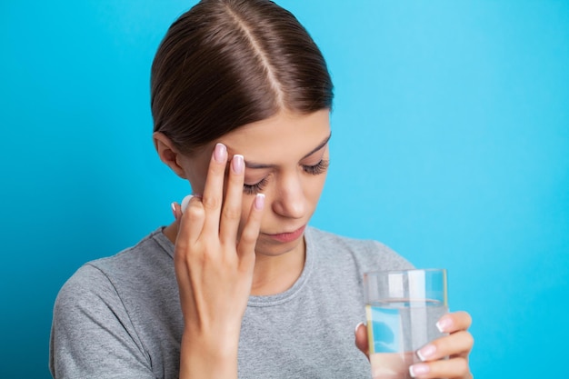 頭痛、腹痛から薬を飲んだり、ビタミンを摂取したりする錠剤とガラスの水を保持している女性