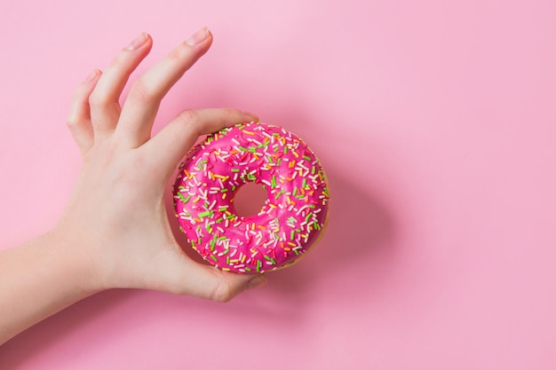 Woman holding pink donut on pink background. Pink donut in hand